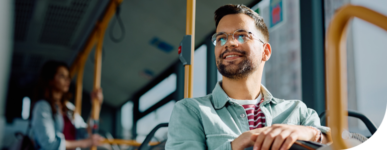 A man is sitting on a bus looking out of the window and smiling